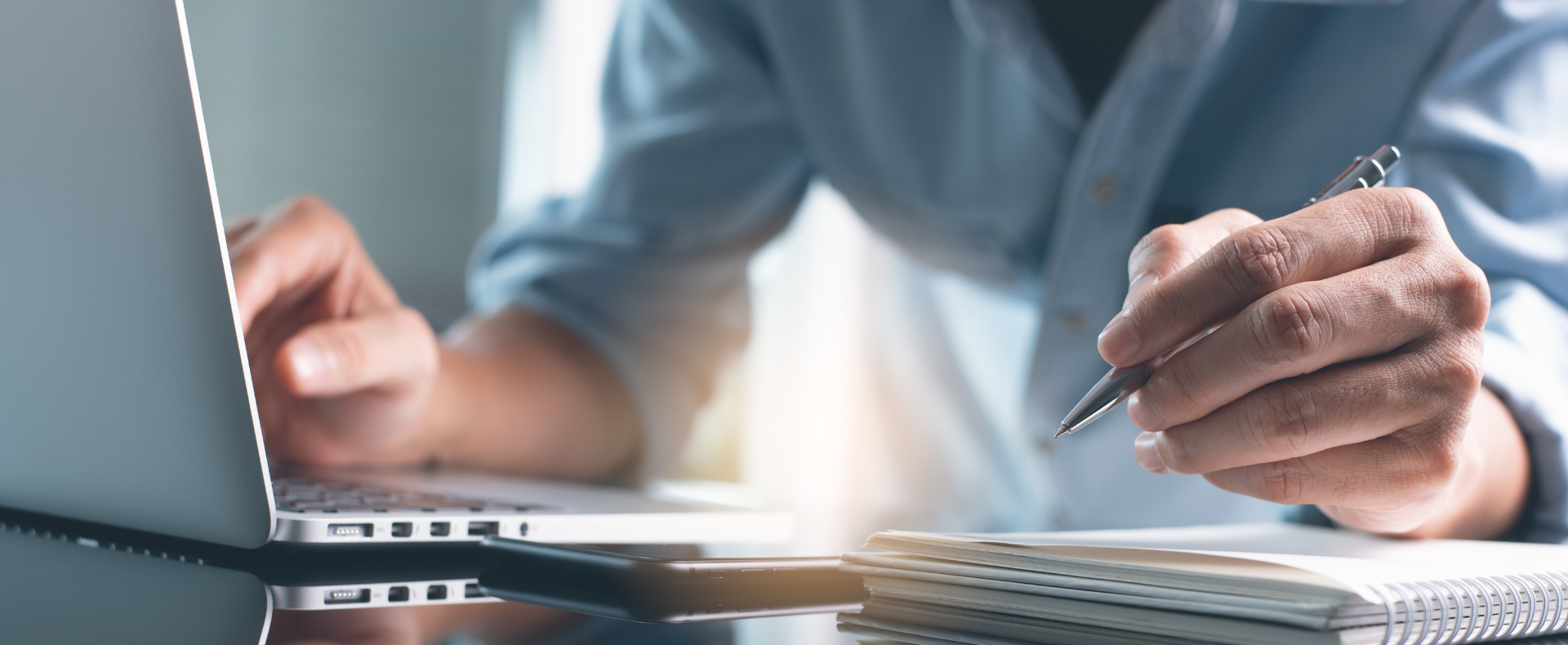 Persona che prende appunti su un blocco note mentre utilizza un laptop