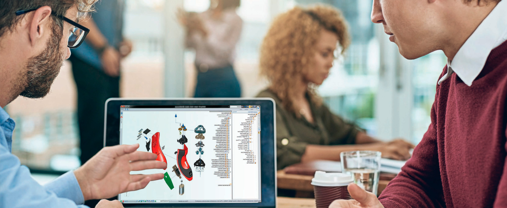 Due colleghi esaminano attentamente un modello 3D su un computer portatile, mentre altri lavorano sullo sfondo
